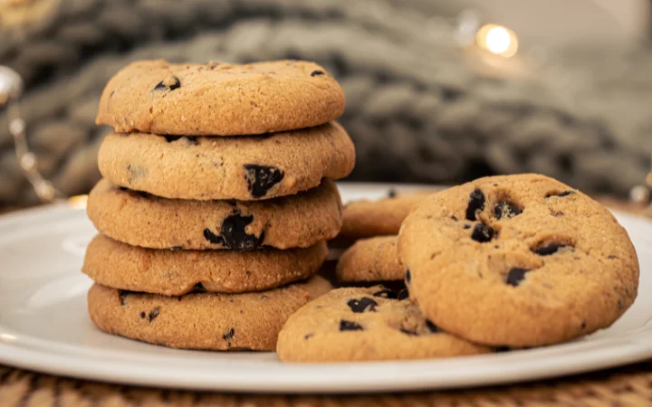  A warm, inviting scene of freshly baked cookies on a cooling rack. The cookies are golden brown, studded with melted chocolate chips that glisten, exuding a homemade and comforting feel.