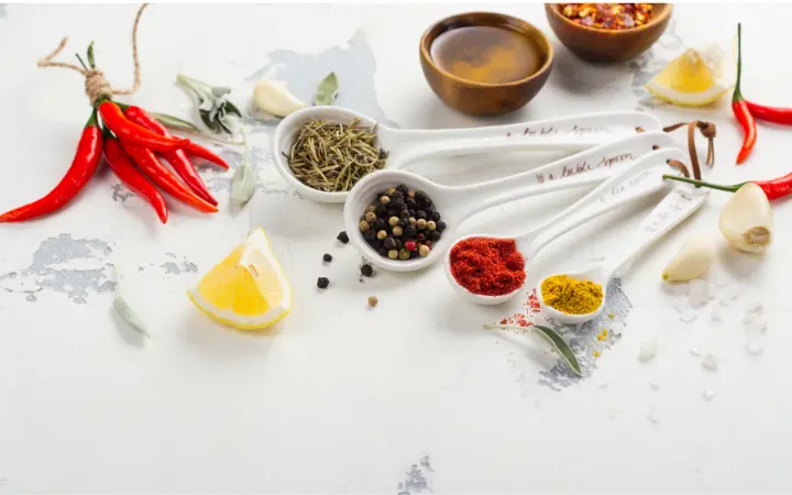 A rustic kitchen table spread with various fresh ingredients for Chimichurri, including parsley, cilantro, garlic, and different oils and vinegars, illustrating the sauce's simplicity and freshness.