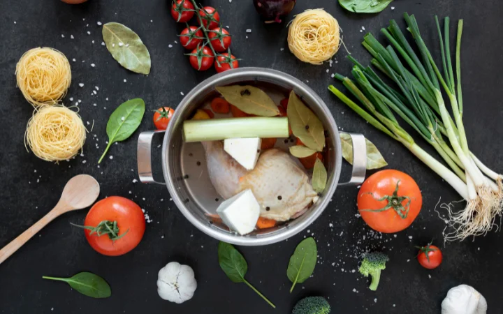 A rustic kitchen counter displaying essential ingredients for Chicken Gnocchi Soup in a crockpot. Visible are fresh chicken breasts, a variety of vegetables like carrots and celery, garlic, herbs, and a packet of gnocchi, all arranged neatly for preparation.