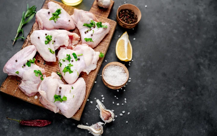 An arrangement showcasing key ingredients for chicken soup: a whole chicken, onions, carrots, celery, and fresh herbs like parsley and thyme. In the background, a chef’s knife and cutting board suggest the preparation process.