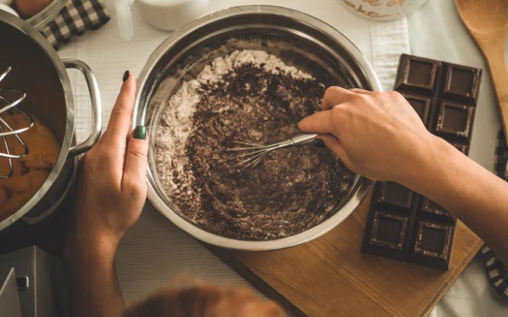 A baker's hands gently folding dry ingredients into a creamy chocolate pound cake batter, with a focus on the texture and consistency of the mix.