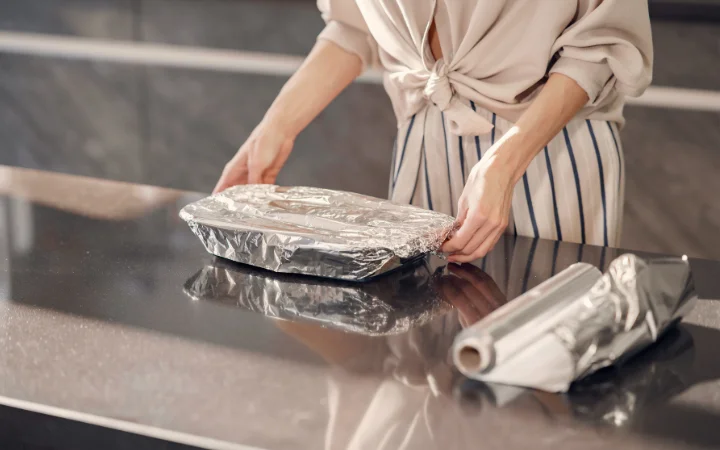  A dessert being wrapped in aluminum foil showcasing Chocolate Pound Cake Storageand, placed in a freezer, with visible frost and ice crystals.