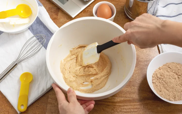 A baker's hands creaming butter and sugar in a mixing bowl, showcasing the texture and consistency of the mixture.