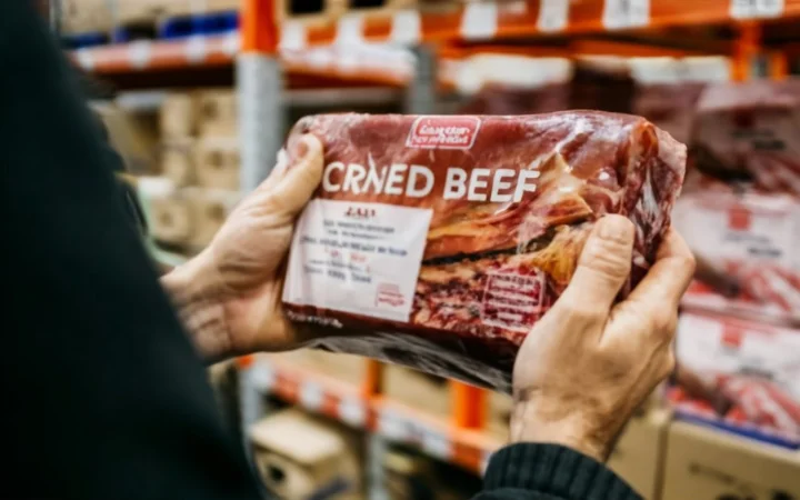 Happy customers shopping for corned beef at Costco, with one customer holding a package and reading the label.