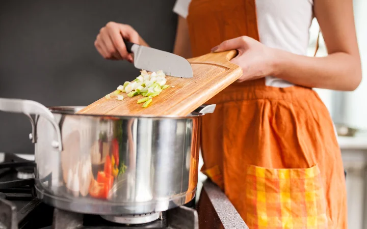 A kitchen scene showing the process of sautéing onions, celery, and garlic, with a variety of herbs and spices on the side.