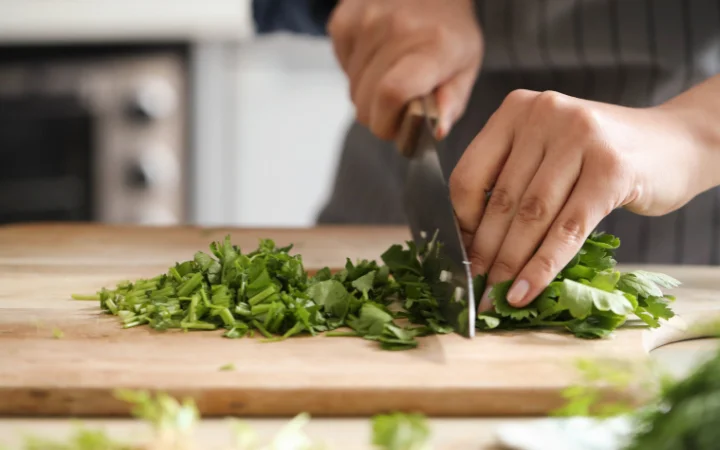 Hands finely chopping fresh herbs on a wooden cutting board