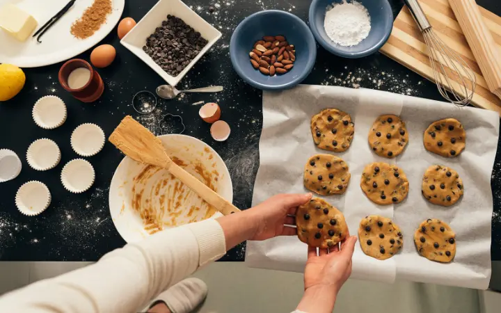 Hands skillfully preparing Nestle chocolate chip cookie dough, with baking tools and ingredients around, emphasizing the art of baking.