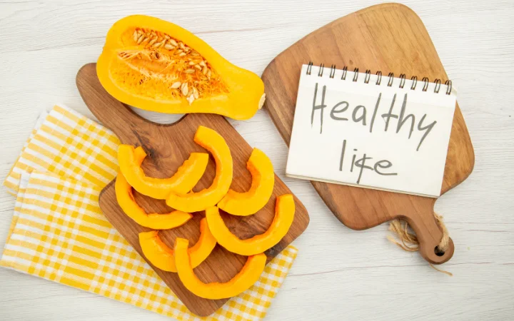  chopped butternut squash on chopping board on yellow white checkered kitchen towel healthy life written on notepad 