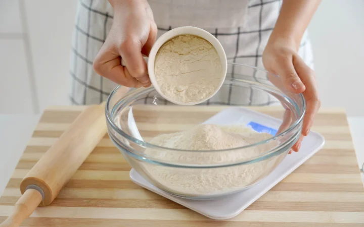 A baker measuring flour accurately with a measuring cup, emphasizing the precision in the process.