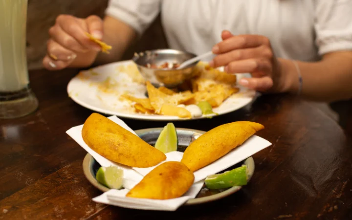 Photo closeup of 3 colombian empanadas and an unfocused woman in the background eating