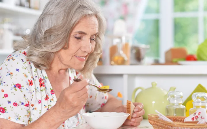 A heartwarming scene of a grandma enjoying a bowl of vegetable soup in a dining table, with a window view showing a garden.