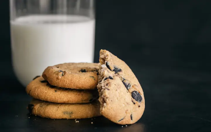 A close-up of a freshly baked Nestle chocolate chip cookie, with a glass of milk in the background, symbolizing the timeless appeal and comfort.