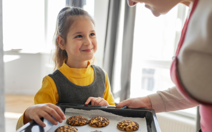 itchen scene where a family is baking together using Ghirardelli chocolate chips. The image shows a warm, inviting kitchen with a batch of cookies in the oven, a bowl of Ghirardelli chocolate chips on the counter, and a family (adults and children) enjoying the baking process together, emphasizing the warmth and joy of home baking with quality ingredients.