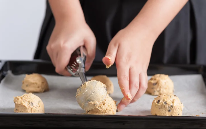 Hands gently mixing cookie dough in a bowl, with focus on achieving the perfect texture, next to an oven with a timer set.