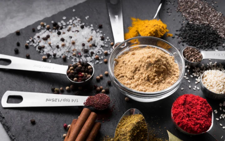 Close-up of essential spices including mustard seeds, coriander seeds, black peppercorns, and bay leaves, each in separate small bowls.