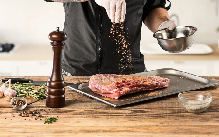 A chef in the kitchen preparing corned beef , showcasing a brisket with good fat marbling, rubbed with pickling spices and ready to be vacuum-sealed.