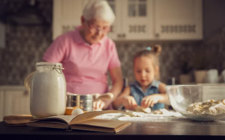 An old, well-loved recipe book open to a page of cookie recipes, with family photos in the background, symbolizing the passing down of traditions.