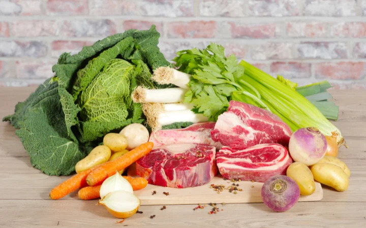 A market scene with fresh vegetables like carrots, potatoes, cabbage, and two types of beef brisket (flat cut and point cut), highlighting the importance of fresh ingredients.