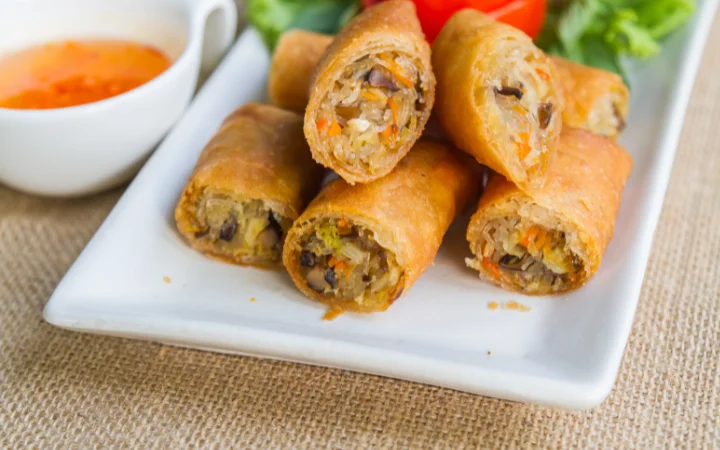 A beautifully set dining table with egg rolls served with dipping sauces, side salads, and drink pairings, showcasing a perfect meal setup.