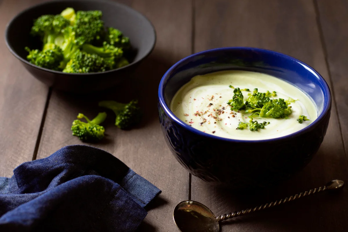 Image of a warm, inviting kitchen scene with a simmering pot of Broccoli Cheddar Soup on the stove. The ingredients like fresh broccoli, cheddar cheese, and spices are displayed on the countertop, emphasizing the soup's comforting nature and its blend of taste and nostalgia.