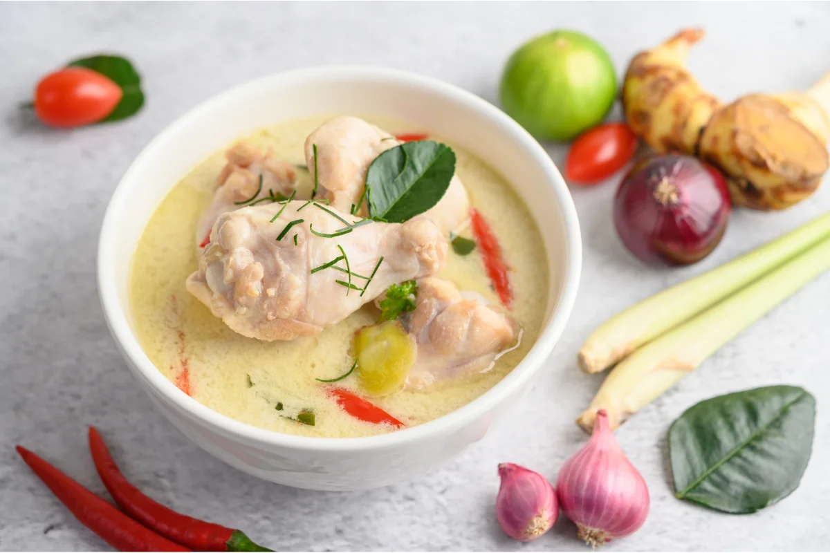 A cozy kitchen scene with a steaming pot of chicken soup on the stove. Ingredients like fresh vegetables, herbs, and a whole chicken are spread out on the counter. The warm lighting and homely atmosphere highlight the comforting essence of making chicken soup.