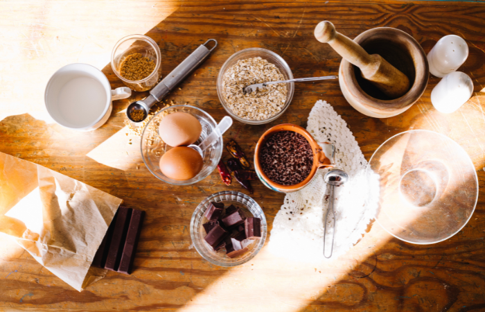 Kitchen counter with ingredients for chocolate chip cookies and an open recipe book, featuring flour, sugars, butter, eggs, chocolate chips, in a cozy baking atmosphere