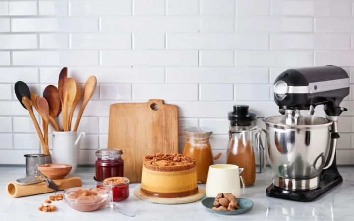 A neatly organized kitchen workspace with all the necessary ingredients for Biscoff cheesecake (cream cheese, sugar, eggs, vanilla extract, Biscoff cookies, and spread) and tools (springform pan, food processor, mixer) laid out.