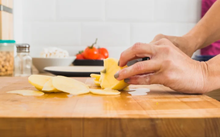 Crop hands cutting potato on board
