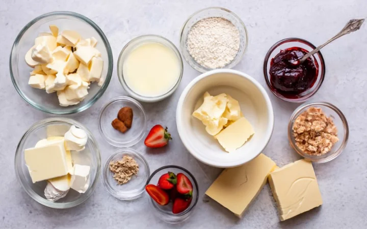 A neatly organized kitchen counter with all the essential ingredients for baking. The scene includes a bowl of softened cream cheese, a jar of strawberry jam with a spoon resting on its side, and a bag of graham cracker crumbs. Nearby, alternative ingredients such as gluten-free flour and vegan cream cheese are also displayed, showcasing the versatility of the recipe.