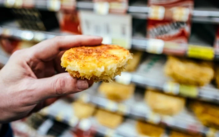 close-up image of a shopper's hand comparing two different brands of frozen hash brown patties in a supermarket freezer aisle. The focus is on the ingredient list and nutritional information on the packaging.