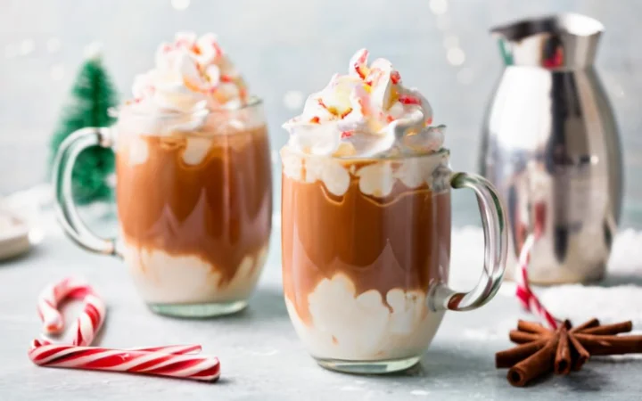 Three versions of peppermint mocha in clear mugs - vegan with almond milk, keto with a sugar substitute, and cold brew - each topped with whipped cream and crushed candy cane, set against a backdrop of a snowy window.