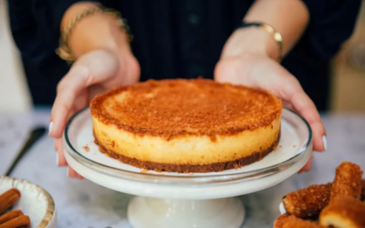 An image showing a joyful moment of serving the churro cheesecake at a gathering. The cheesecake is being sliced, and one piece is being plated, with eager hands and smiling faces in the background, eagerly awaiting their slice. The atmosphere should be festive and warm, highlighting the dessert's role in bringing people together.