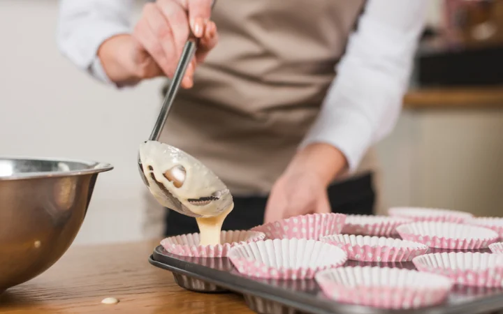 Close-up of female baker pouring mixed cake batter in the cupcake holder