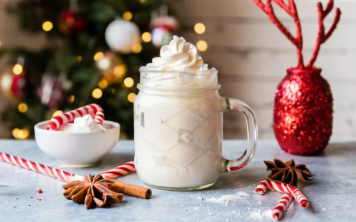  A DIY crafting table with homemade peppermint syrup in a glass jar, whipped cream in a bowl, and crushed candy canes on a plate. In the background, a handcrafted holiday decoration adds to the festive atmosphere.