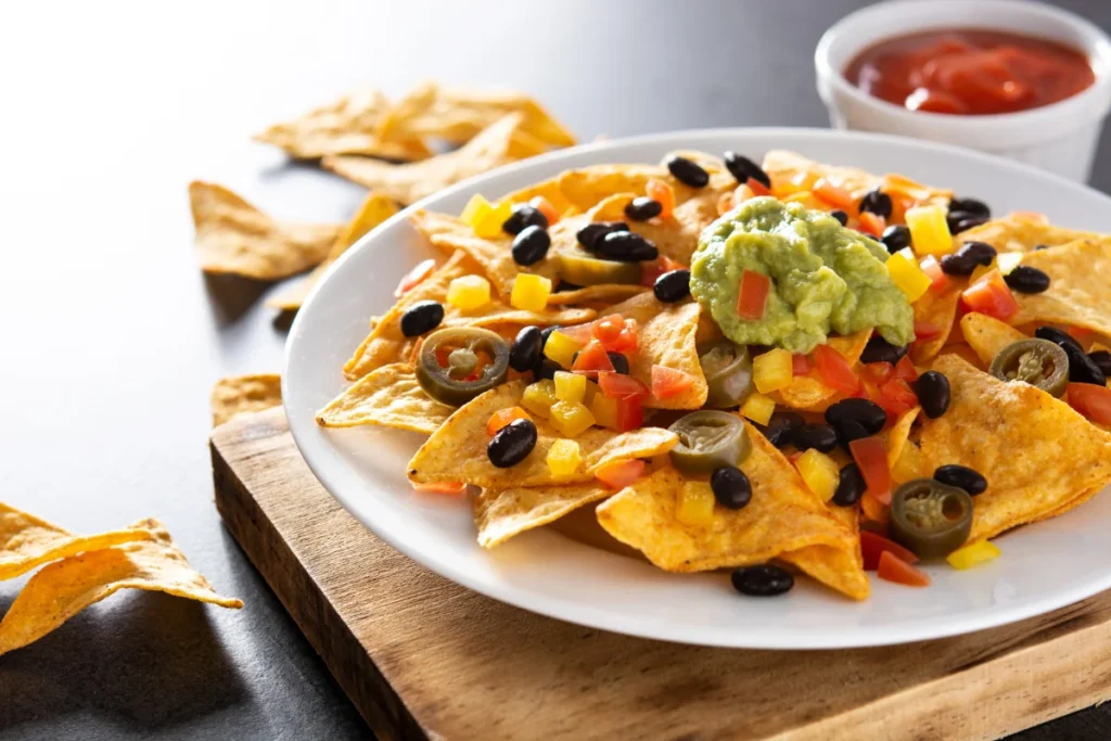 A vibrant, colorful image capturing the essence of nacho fries, showcasing a plate overflowing with golden, crispy fries topped with melted cheese, diced tomatoes, jalapeños, and a drizzle of creamy sauce. The background features a bustling kitchen setting, highlighting the fusion of flavors and textures.